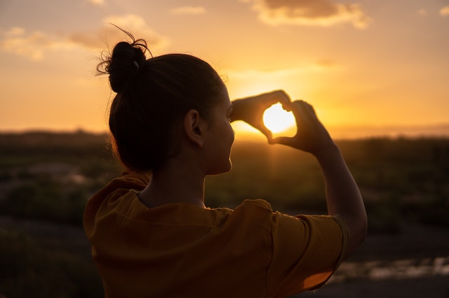 Woman with hands in a heart around a sunset